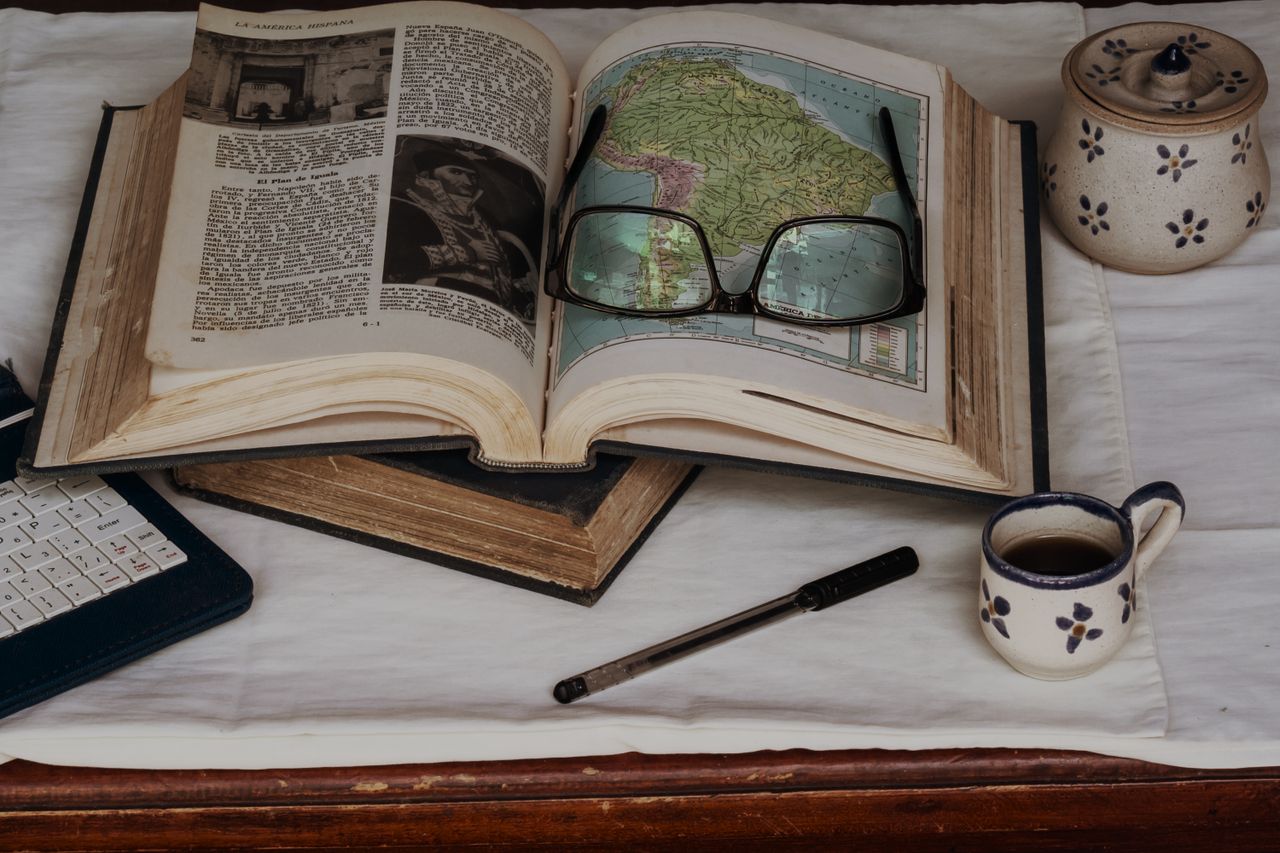 Explore and study with open book, maps, coffee, and glasses, perfect for a quiet afternoon.