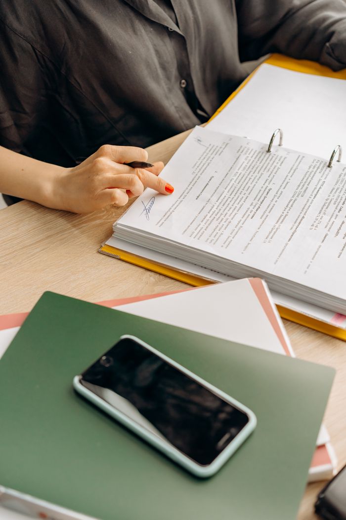 Person reviewing documents at a workplace desk with a smartphone.