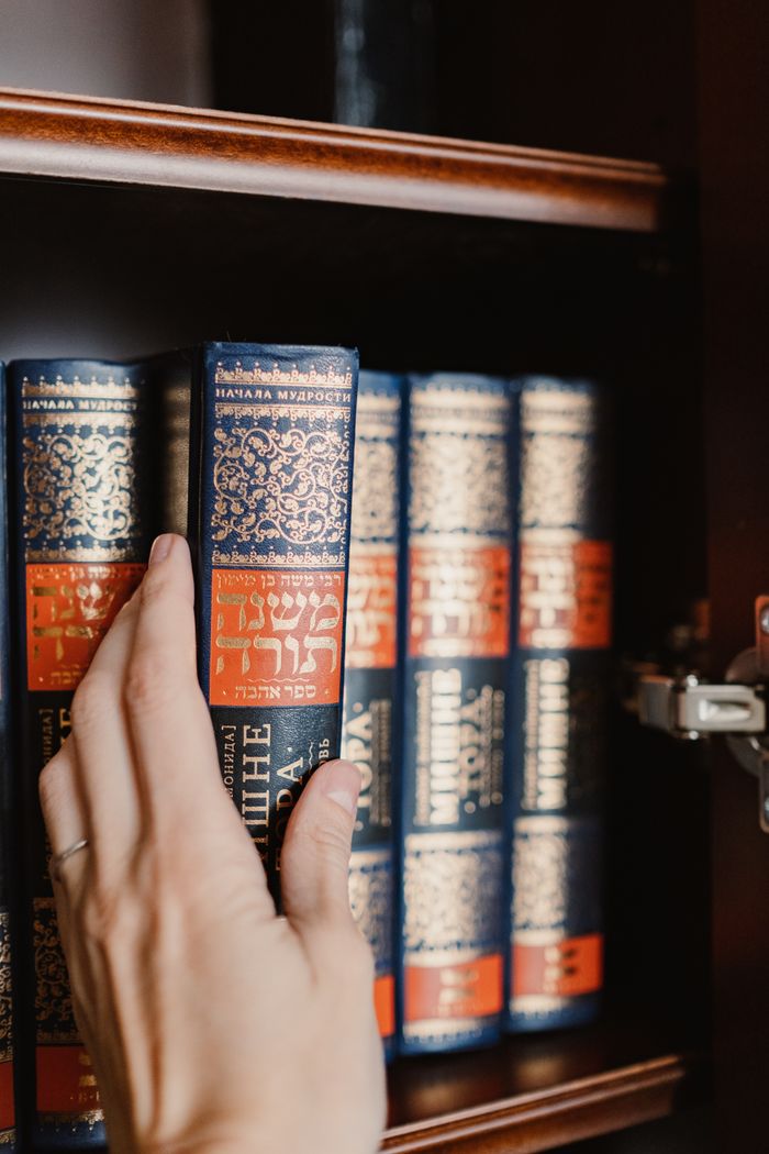 Close-up of a hand reaching for a Torah book on a bookshelf, symbolizing Jewish culture.